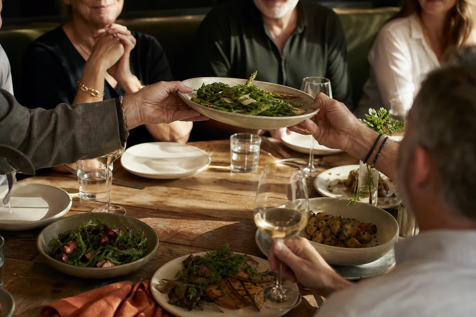 Guests passing a shared plate across a group dining table